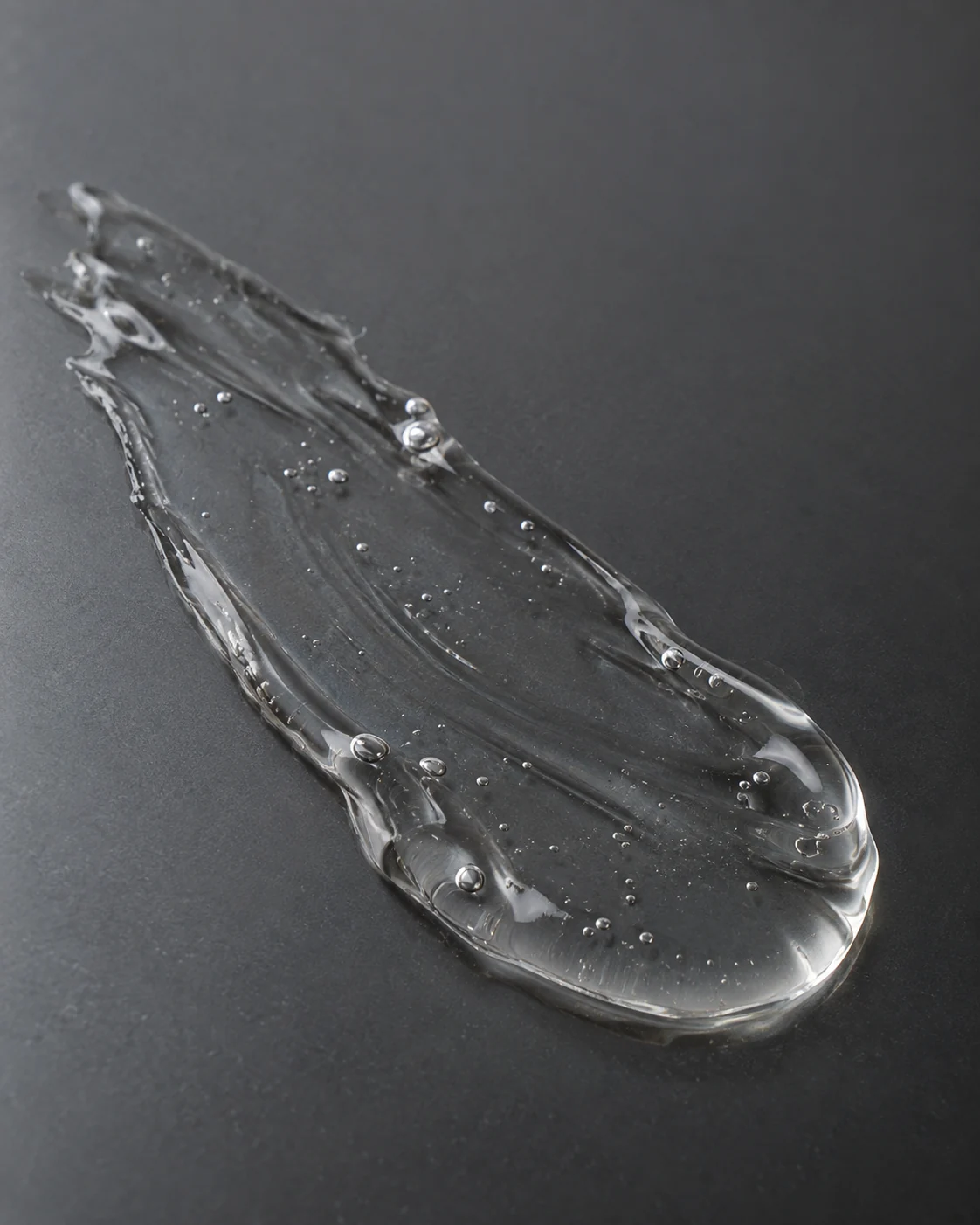 Gel texture study: a thin translucent trail with tiny natural air bubbles on smoke-grey glass